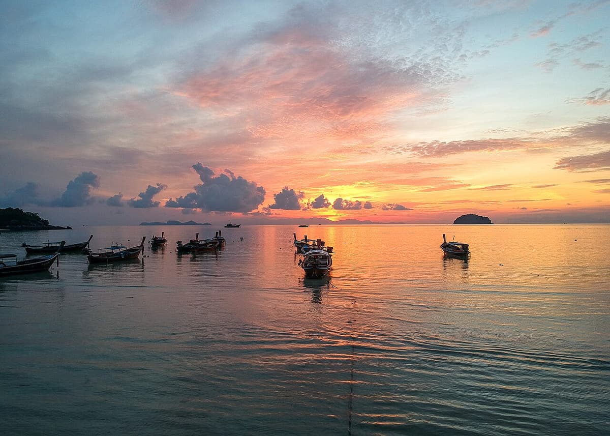 Sunrise over the sea at Koh Lipe with longtail boats moored in the shallows